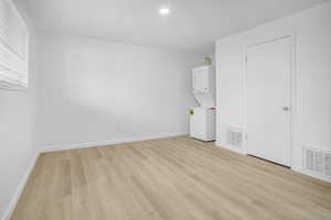 Unfurnished bedroom with stacked washer and clothes dryer, light wood finished floors, and recessed lighting