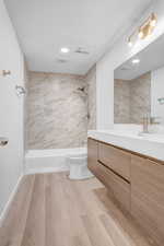 Bathroom with tiled shower, vanity, and light wood-style floors