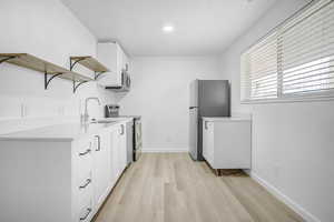 Kitchen with white cabinetry, open shelves, stainless steel appliances, and light wood-style flooring