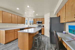 Kitchen featuring a breakfast bar, stainless steel appliances, light countertops, a center island, and dark wood finished floors