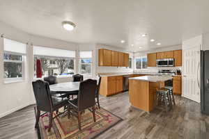Kitchen with light countertops, a center island, a breakfast bar area, stainless steel appliances, and dark wood-style flooring