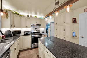 Kitchen with stainless steel appliances, hanging light fixtures, dark stone counters, tasteful backsplash, and cream cabinets