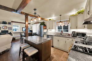 Dual tone kitchen with open floor plan, a breakfast bar area, dark stone counters, pendant lighting, and beamed ceiling