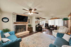 Living area featuring dark wood finished floors, a textured ceiling, a fireplace, a ceiling fan, and a chandelier