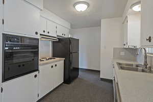 Kitchen with light countertops, black appliances, white cabinets, and a textured ceiling