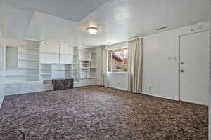 Unfurnished living room with a textured ceiling and dark colored carpet
