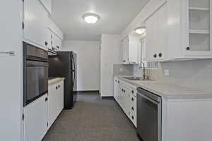Kitchen featuring light countertops, black appliances, backsplash, white cabinetry, and a textured ceiling