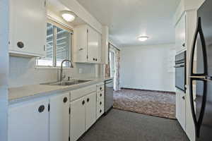 Kitchen with black appliances, light countertops, white cabinets, dark carpet, and decorative backsplash