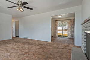 Unfurnished living room with dark colored carpet, a ceiling fan, and a fireplace