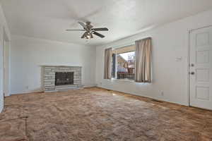 Unfurnished living room with carpet, a ceiling fan, and a stone fireplace