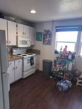 Kitchen with white appliances, white cabinets, dark wood-style flooring, and dark stone countertops