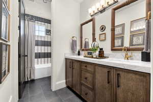 Full bath with shower / bath combo with shower curtain, double vanity, and dark tile patterned flooring