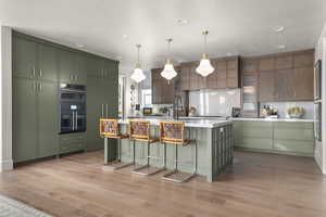 Kitchen with green cabinets, a kitchen bar, a kitchen island with sink, double wall oven, and extractor fan