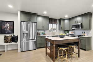Kitchen with green cabinets, stainless steel appliances, light wood-style flooring, tasteful backsplash, and light stone countertops