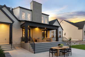 Back of property at dusk featuring an outdoor living / dining area, french doors, a chimney, a patio area, and brick siding