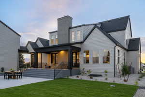 Back of house featuring a yard, a chimney, covered porch, outdoor dining area, and roof with shingles