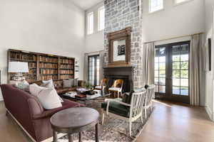 Living room with a stone fireplace, french doors, a high ceiling, and wood finished floors