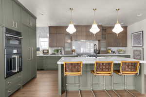 Kitchen featuring a breakfast bar area, a center island with sink, double oven, backsplash, and green cabinets
