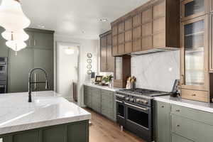 Kitchen with range with two ovens, green cabinets, light stone counters, light wood finished floors, and hanging light fixtures