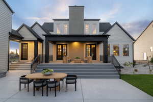 Back of house at dusk featuring outdoor dining area, a patio, a shingled roof, a chimney, and brick siding