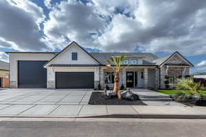 Modern inspired farmhouse with a standing seam roof, covered porch, stone siding, driveway, and a garage