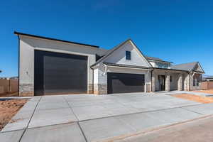 View of front facade featuring stone siding, a standing seam roof, an attached garage, and concrete driveway