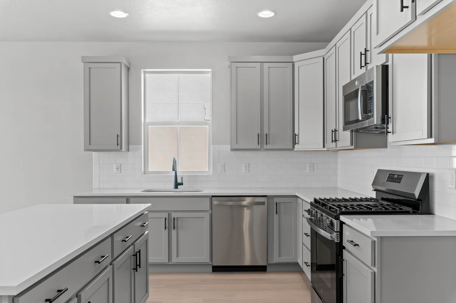 Kitchen featuring stainless steel appliances, gray cabinetry, light wood-type flooring, light stone countertops, and recessed lighting