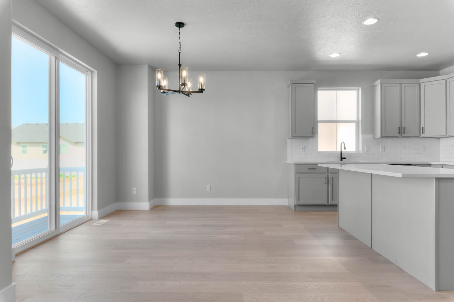 Kitchen with a chandelier, light wood finished floors, gray cabinetry, decorative backsplash, and light stone countertops