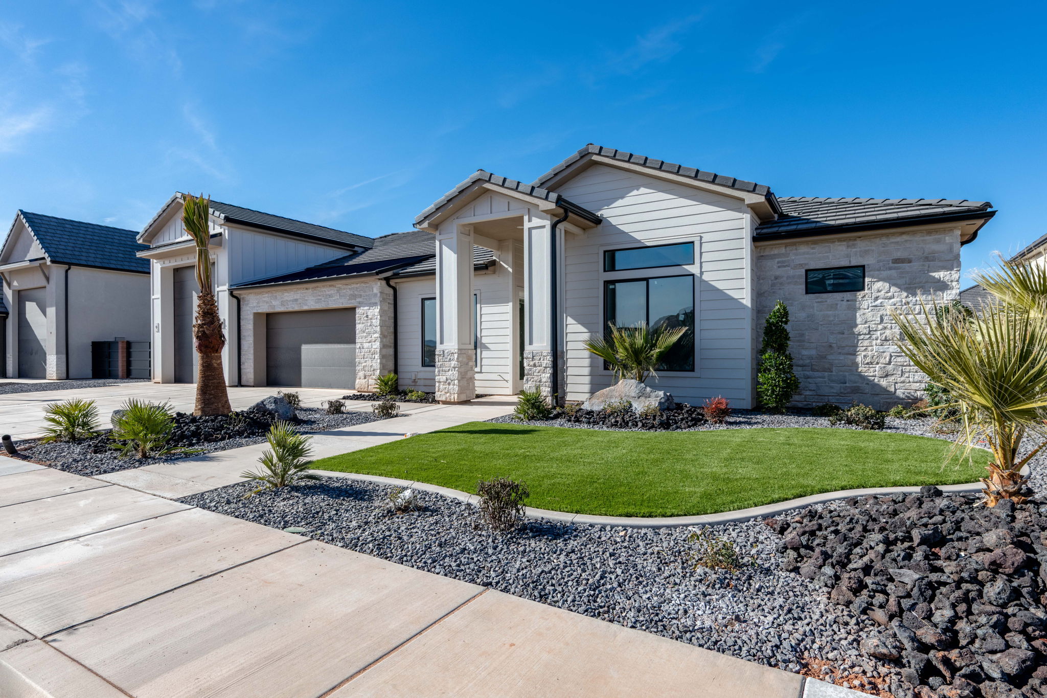 View of front facade with stone siding, a front lawn, an attached garage, concrete driveway, and a tile roof