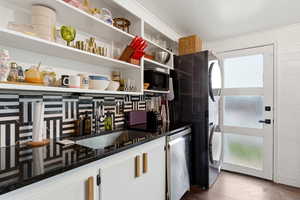 Kitchen with dark stone counters, white cabinets, stacked washer and dryer, dark wood finished floors, and stainless steel dishwasher
