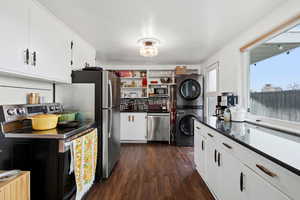 Kitchen featuring white cabinets, stainless steel appliances, dark wood-type flooring, stacked washing machine and dryer, and dark countertops
