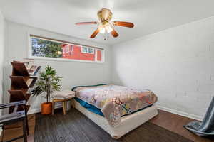 Bedroom featuring dark wood-style floors, ceiling fan, and brick wall
