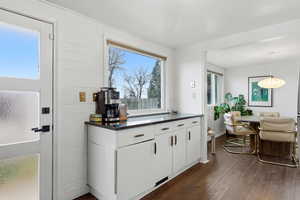 Kitchen with white cabinetry, dark wood-style floors, decorative light fixtures, and dark stone counters
