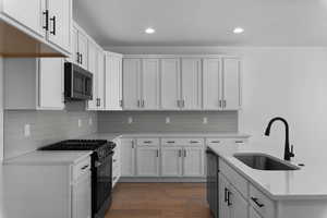 Kitchen featuring black gas range oven, white cabinets, light wood-style floors, light stone countertops, and stainless steel microwave