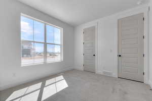 Unfurnished bedroom with light colored carpet and baseboards