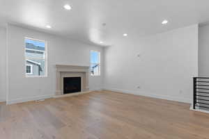 Unfurnished living room featuring a fireplace with raised hearth, light wood-style floors, and recessed lighting