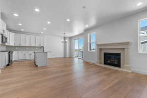 Kitchen with open floor plan, white cabinetry, gas range oven, backsplash, and a glass covered fireplace