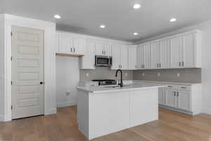 Kitchen with white cabinets, light wood-type flooring, stainless steel appliances, a center island with sink, and recessed lighting