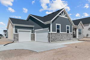 View of front of property featuring stone siding, an attached garage, board and batten siding, and driveway