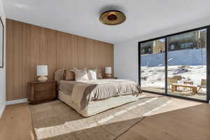 Bedroom featuring wooden walls, access to exterior, light wood-style flooring, and an accent wall