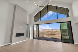 Unfurnished living room with a mountain view, a glass covered fireplace, vaulted ceiling, and light wood-style floors