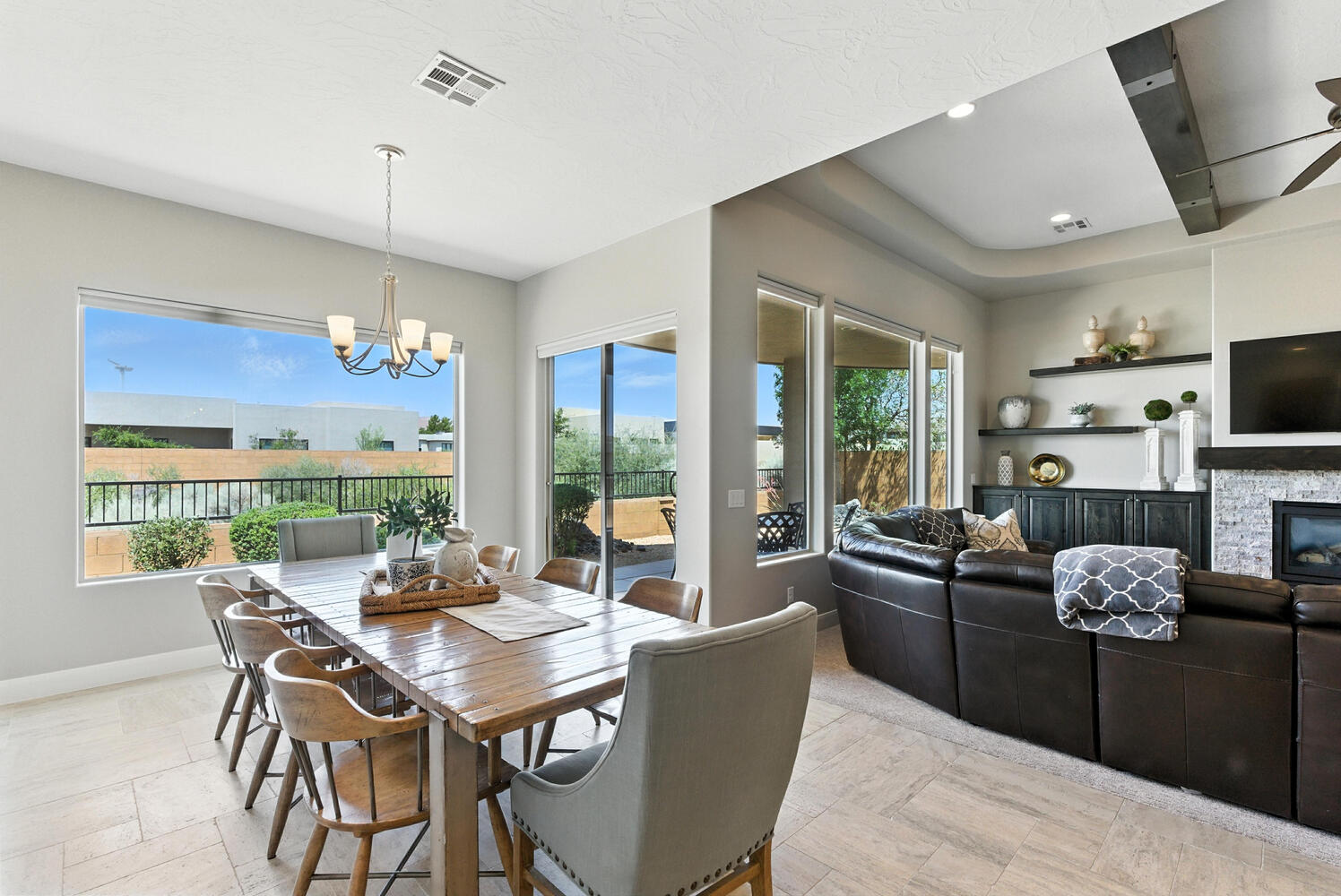 Dining room featuring suspended lighting, a stone fireplace, a ceiling fan, and light stone finish floors