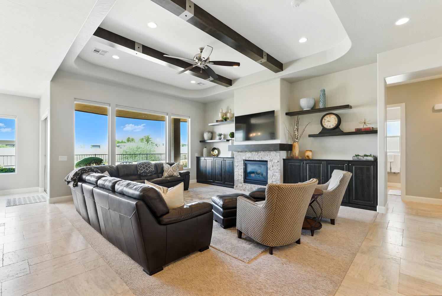 Living area featuring recessed lighting, a raised ceiling, a ceiling fan, a stone fireplace, and light stone finish flooring