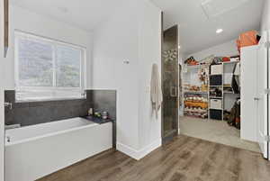 Full bathroom with a shower stall, a walk in closet, dark wood finished floors, a garden tub, and lofted ceiling