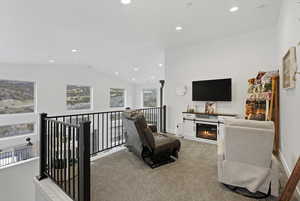 Living area featuring light colored carpet, a glass covered fireplace, vaulted ceiling, and recessed lighting