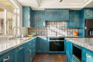 Kitchen with blue cabinetry, stainless steel appliances, a tray ceiling, and tasteful backsplash