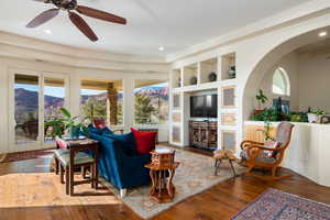 Living area with ceiling fan, built in features, wood-type flooring, and arched walkways