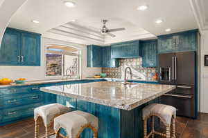 Kitchen featuring a kitchen breakfast bar, wood tiled floors, high quality fridge, blue cabinetry, and a raised ceiling