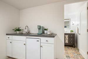 Bar area with white cabinetry, dark countertops, and white fridge