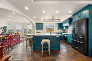 Kitchen with high end refrigerator, blue cabinetry, a kitchen bar, ceiling fan, and a raised ceiling
